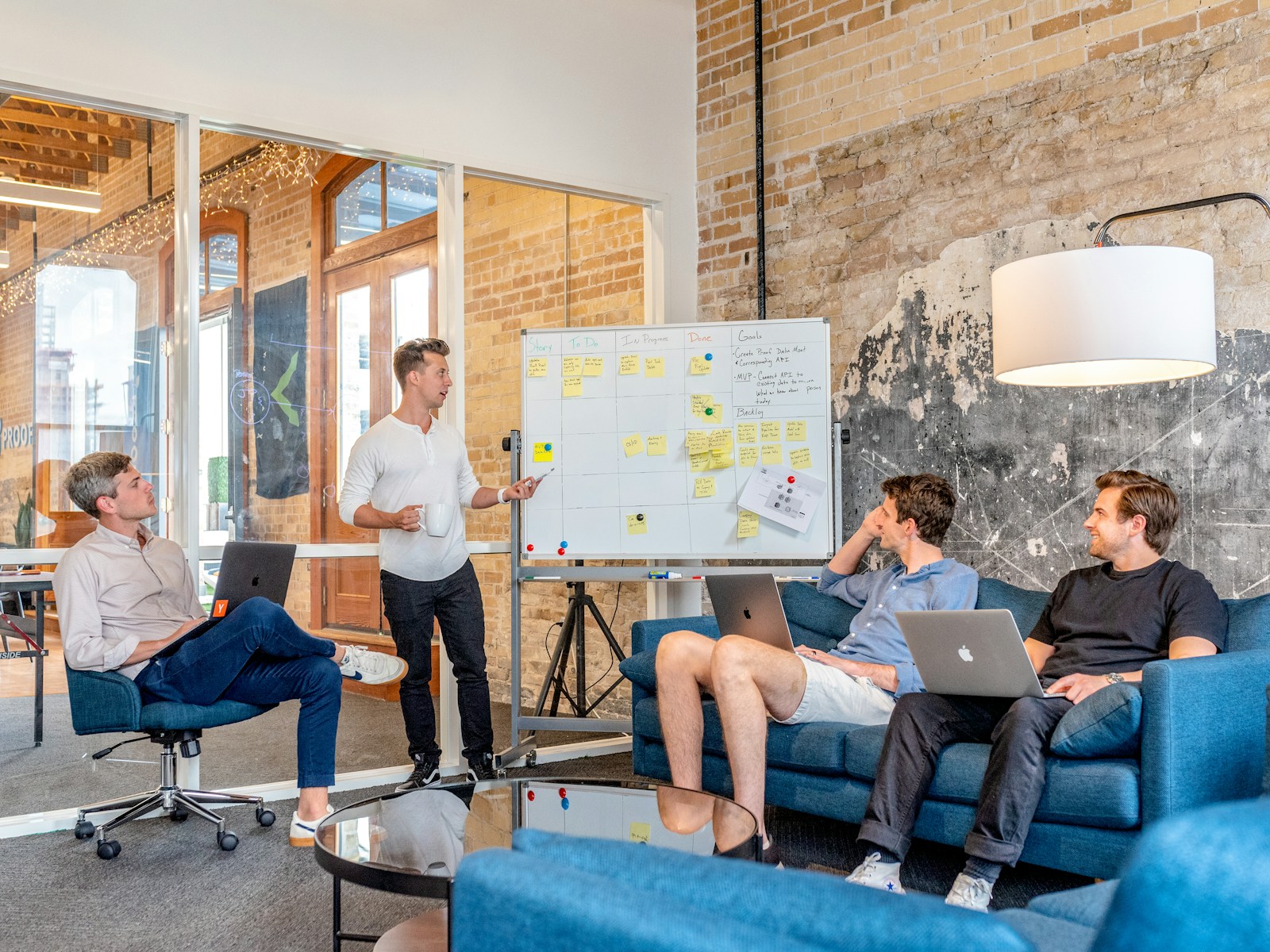 three men sitting while using laptops and watching man beside whiteboard, business plan